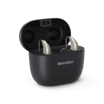 A pair of beige hearing aids sit in an open Bernafon Charger Plus miniRITE case with the Bernafon logo on the front, all set against a plain white background.