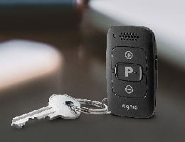 A pair of silver keys is attached to a black Signia miniPocket device with multiple buttons, including a P button, shown on a smooth dark surface.